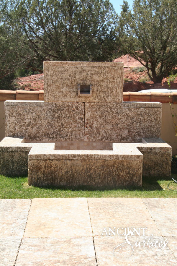 Monolithic reclaimed limestone wall fountain with a recessed square spout and flanking stone benches on a desert terrace