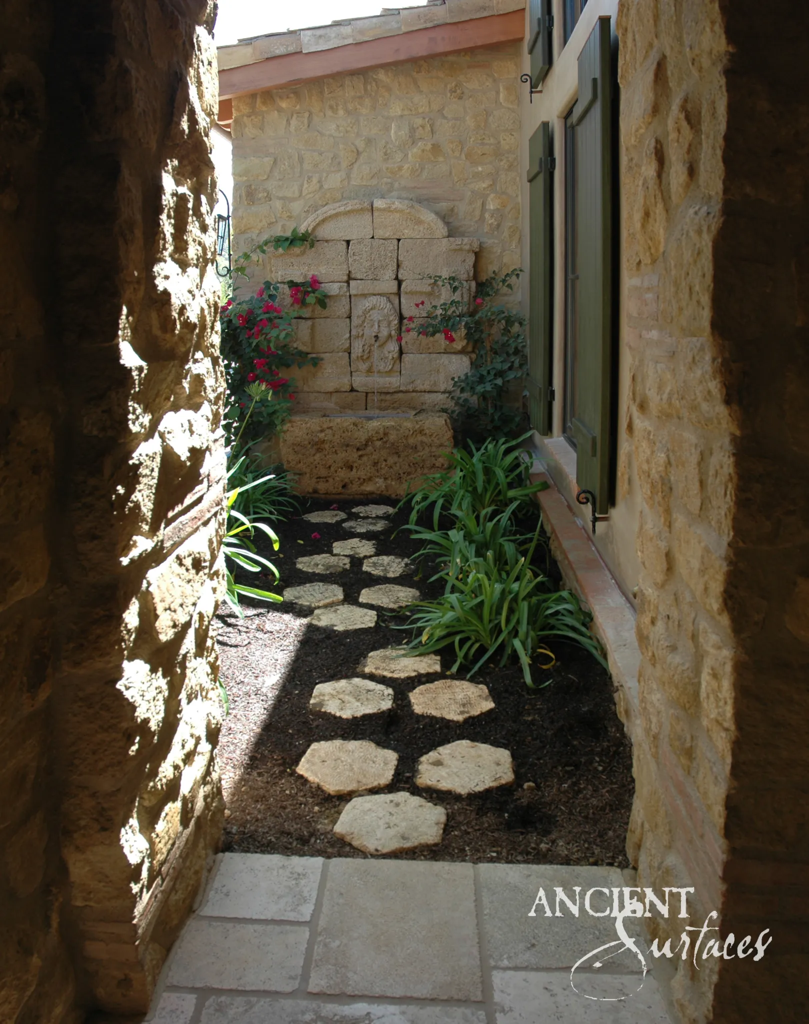 Reclaimed limestone wall fountain with a carved mask spout in an ashlar niche, installed in a planted side garden